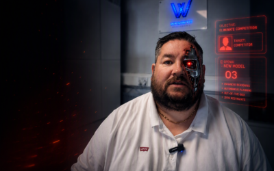 - WYSIWYG Computers Man with a cyborg half-face and glowing red eye in a dim lab, with a red holographic monitor to his right.