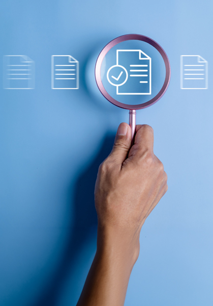 Policies - WYSIWYG Computers Hand holding a magnifying glass over a document icon with a checkmark, symbolizing document verification or audit.